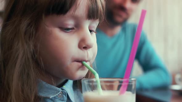 A Little Girl Drinking a Milkshake From a Tube in a Cafe, Close-up.