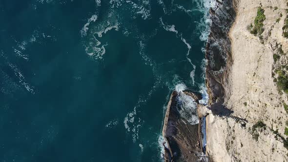 Aerial Top View of Waves Break on Rocks in a Blue Ocean