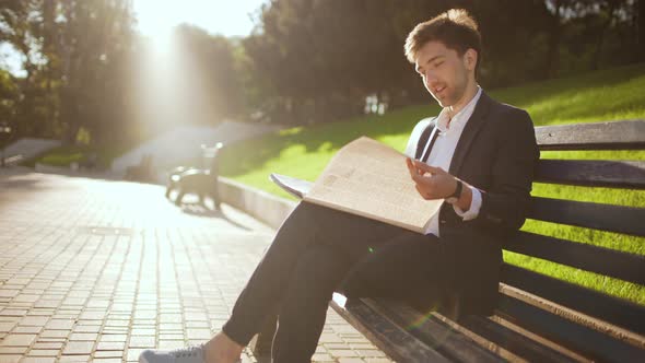 Slow Motion of Handsome Boss Business Man in Suit Sitting on Bench in Green City Park Finish Reading