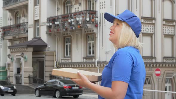 Rear View Shot of a Delivery Woman Looking Around on the Street Holding Pizza Box alt