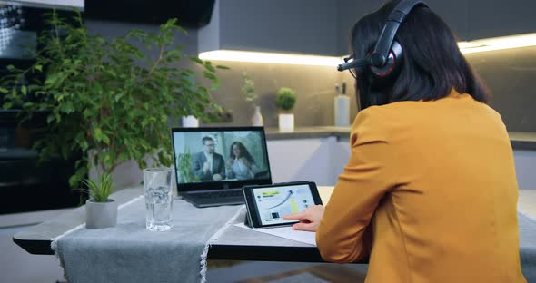 Woman in Headset in Orange Jacket Sitting in front of Computer During Video Meeting alt