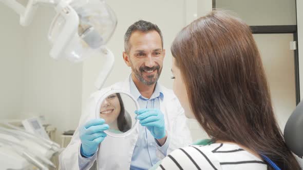 Cheerful Mature Dentist Holding a Mirror for His Female Patient