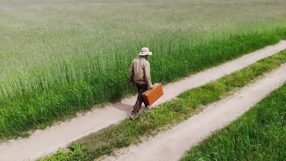 Man Alone Walking By Country Road in a Green Field, Holding Suitcase in a Hand, Funny Travel Concept