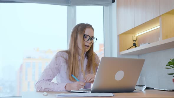 Young woman actively works on a laptop at home, actively communicates with a client. alt