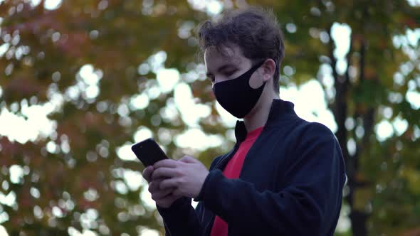 Portrait Boy in Protective Medical Mask Walks Down To the Street Uses Phone Texts Scrolls Surfs the