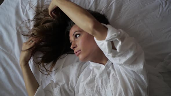 Sexy Brunette Girl Lies on a White Bed Plays with Her Hair alt