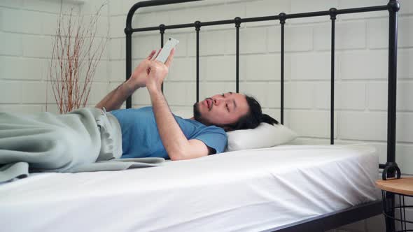 Asia male turn off alarm clock in mobile phone after awake on bed alt