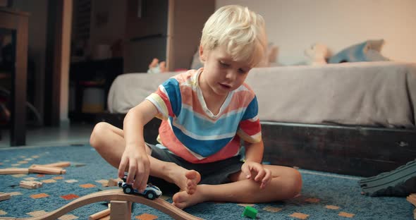 Child Boy Playing with Toy Car on Wooden Railway Road in Living Room on Evening alt