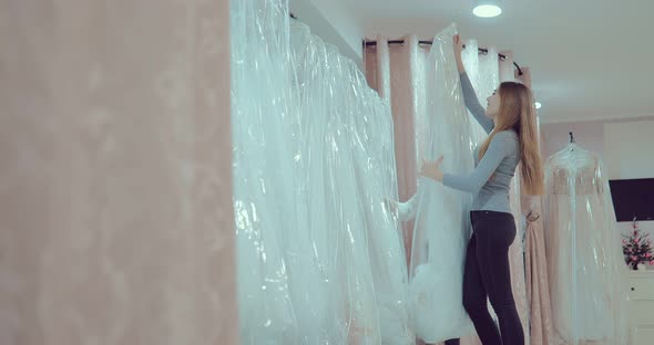 Happy and Beautiful Girls Take the Wedding Dress From the Hanger and Look at It alt