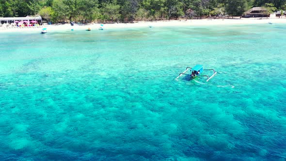 Traditional Balinese boat turning around in the crystal clear sea water near the white sandy beach alt