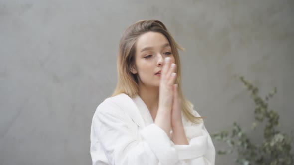 Beautiful Young Woman in Bathrobe Enjoying Condition of Skin on Hands After Applying Cream in