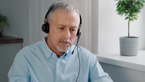 An Elderly Businessman Wearing Headphones Participates in Online Negotiations