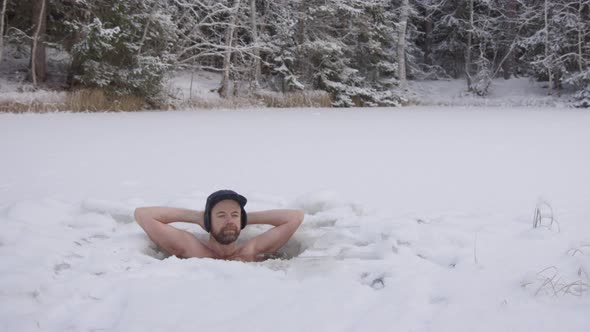 ZOOM OUT - An ice bather finishes his daily practice and steps out of his snowy ice hole alt