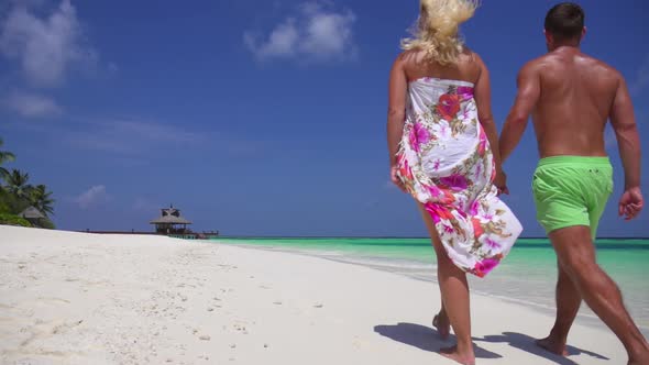 A couple walks on the beach holding hands at a tropical island resort hotel alt
