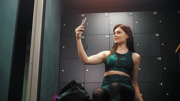 Young Pretty Sportive Woman Taking a Selfie with Her Phone in the Locker Room alt