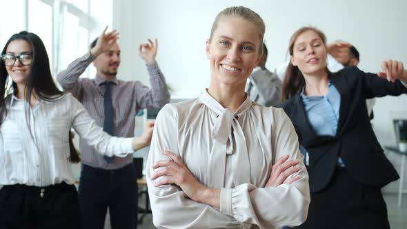Joyful Blond Lady Smiling at Camera Standing in Workplace Where Businesspeople Dancing Having Fun alt