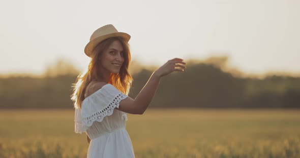 Pretty Young Woman Throws Her Hat and Runs Through a Green Meadow. Happy Girl Whirls and Jumps in