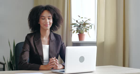 Woman in Business Style Attire Sits at Working Table in Office Room with Laptop Device, Looks at alt