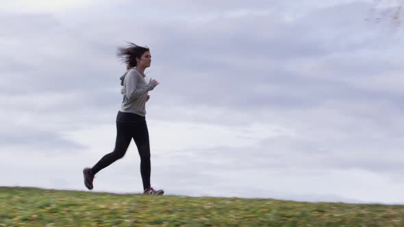 Panning view of woman on hilltop jogging past tree alt