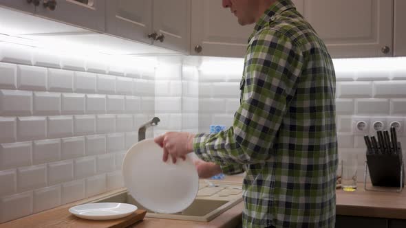 Young Man in Plaid Shirt Washing Dishes on the Kitchen at Home