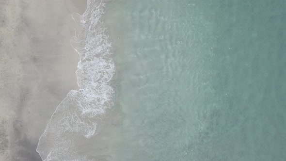 Aerial top down footage of foaming breaking waves on white, black sand Virgin Beach, Bali, Indonesia