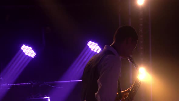 Silhouette a Young Stylish Guy Plays the Golden Shiny Saxophone in the Purple Spotlights on Stage alt