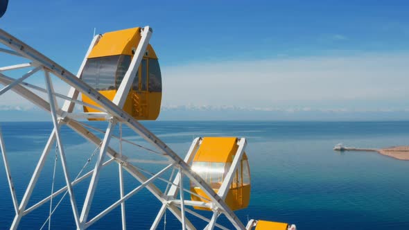 The bright yellow cabin of the white Ferris wheel attraction, standing over a huge lake alt