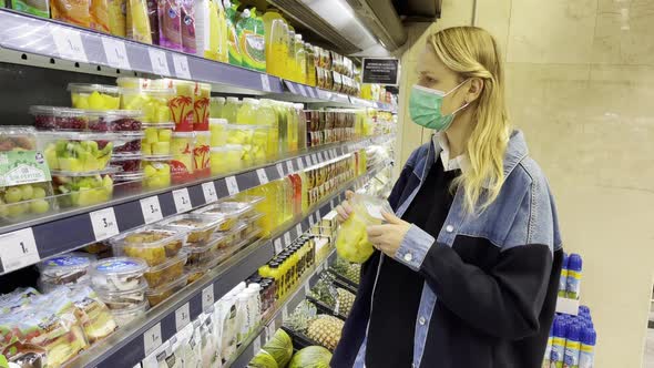 Woman in mask buying cut fruits in supermarket alt