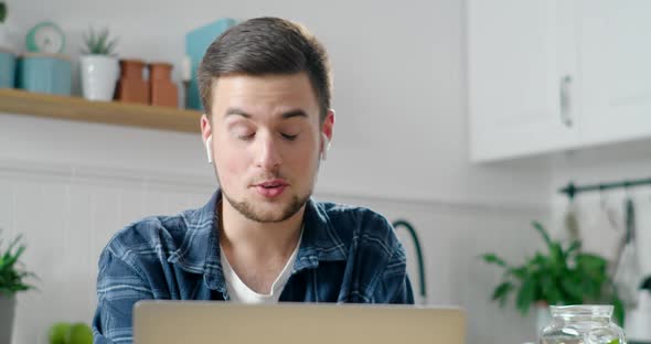 Man in Wireless Earphones Talks Online By Video Call on Laptop in Kitchen alt