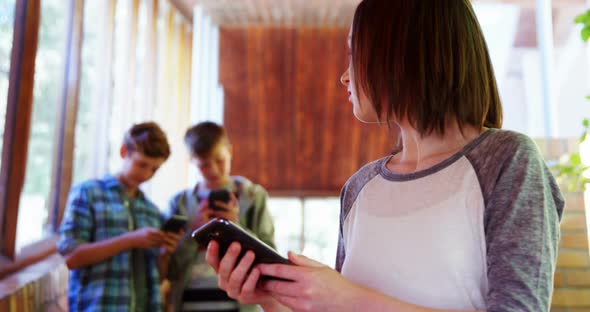 Schoolgirl using mobile phone in corridor at school alt