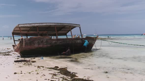 African Fishermen Cleans a Boat From Algae on the Shore at Low Tide Zanzibar alt