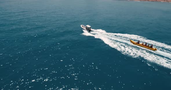 Drone Follows Motor Boat with Enjoying People on Inflatable Banana at Summer Day alt