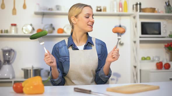 Pretty Girl Choosing Cucumber Instead Sausage, Low-Calorie Food vs Carbohydrates alt
