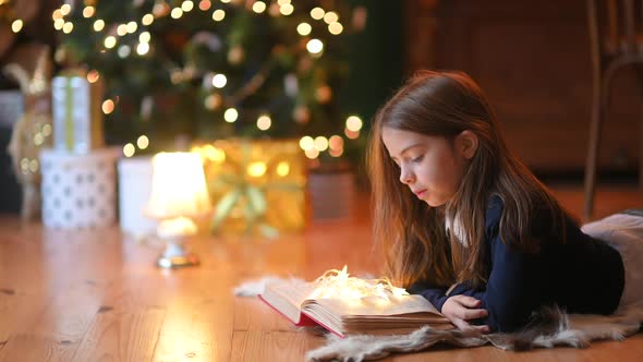 girl lies on the floor against the background of a festive Christmas tree and reads a book
