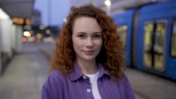 Young woman standing at train station, looking at camera