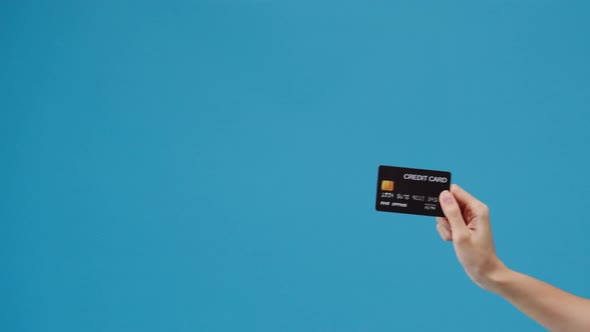 Young woman hand shows credit card for shopping online over blue background in studio.