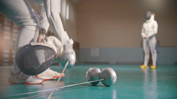 Two Young Women Fencers Having a Training in the Gym - A Woman Takes the Helmet on the Foreground alt