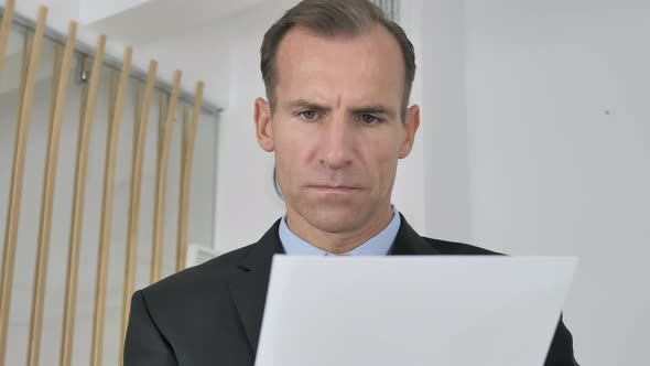Pensive Middle Aged Businessman Reading Documents in Office, Paperwork alt