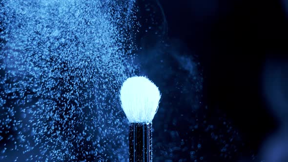 Blue Neon Glowing Ultraviolet Powder on a Makeup Brush Flying Away with Beautiful Vintage Bokeh alt