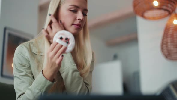 Smiling blond woman powder the face with a sponge alt
