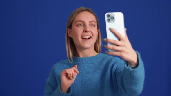 Smiling woman wearing blue sweater talking by video call on phone alt