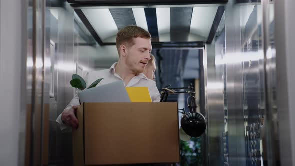 A Man Holds a Box with His Belongings While Choosing in the Elevator alt