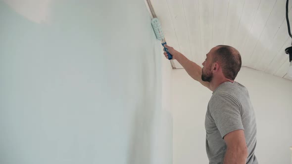 Caucasian Man Paints the Wall with a Roller Man Stands on a Stepladder Dad Makes Repairs in the Room alt