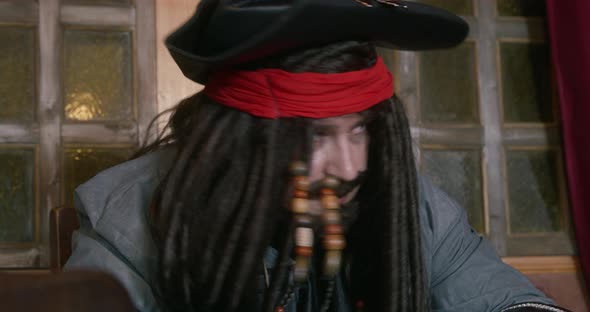 Pirate in a Tricorn Hat and in a Wig with Dreadlocks Decorated with Beads Looks Around Making Sure