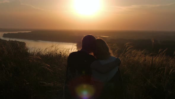 silhouette of a couple sitting in a field with a view of the river and sunset