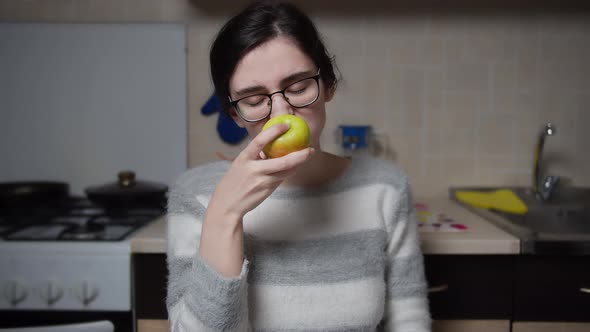 Serious Girl Bites Off an Apple in the Kitchen and Looks at the Camera