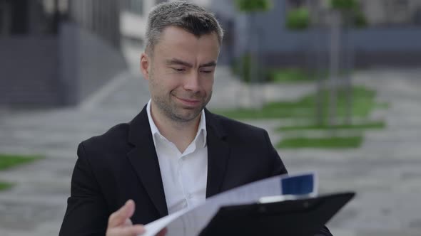 Close Up View of Male Person in Wheel Chair Looking Through Financial Report at City Street alt