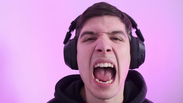 Closeup of a Man Wearing Large Headphones Looking Into the Camera and Showing His Teeth Against a alt