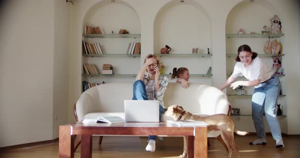 Tired Wife Sitting on the Couch Annoyed While a Noisy Little Daughter Screams Jumps on the Couch and alt