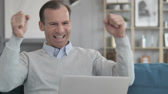 Middle Aged Man Celebrating Success on Laptop at Creative Office alt